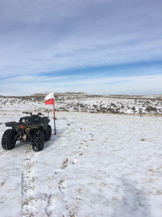 An ATV parked beside a surveyor's flag on snow-covered eastern Wyoming rangeland