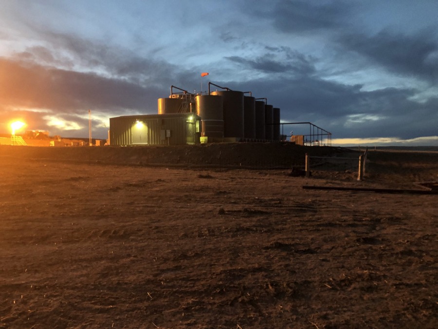 A produced water tank battery lit against a dusk sky on open ground