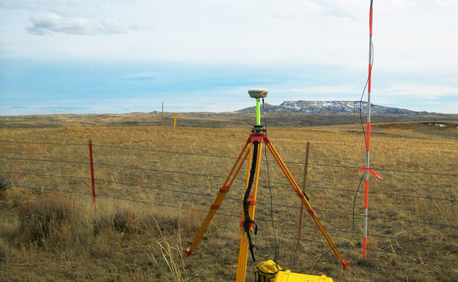 A survey GPS receiver set up on a tripod on open Wyoming rangeland below a snow-covered butte