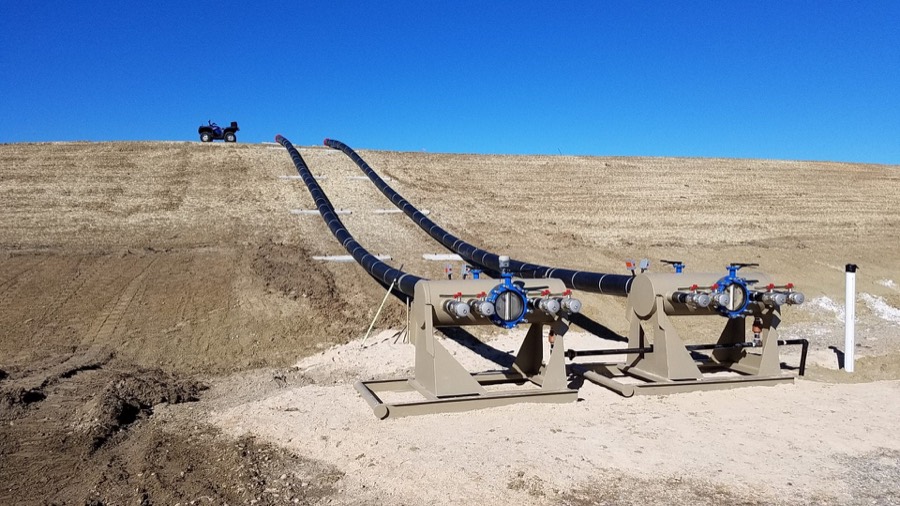 Two water transfer loadout manifolds with valves, feeding twin HDPE lines up over a graded bank