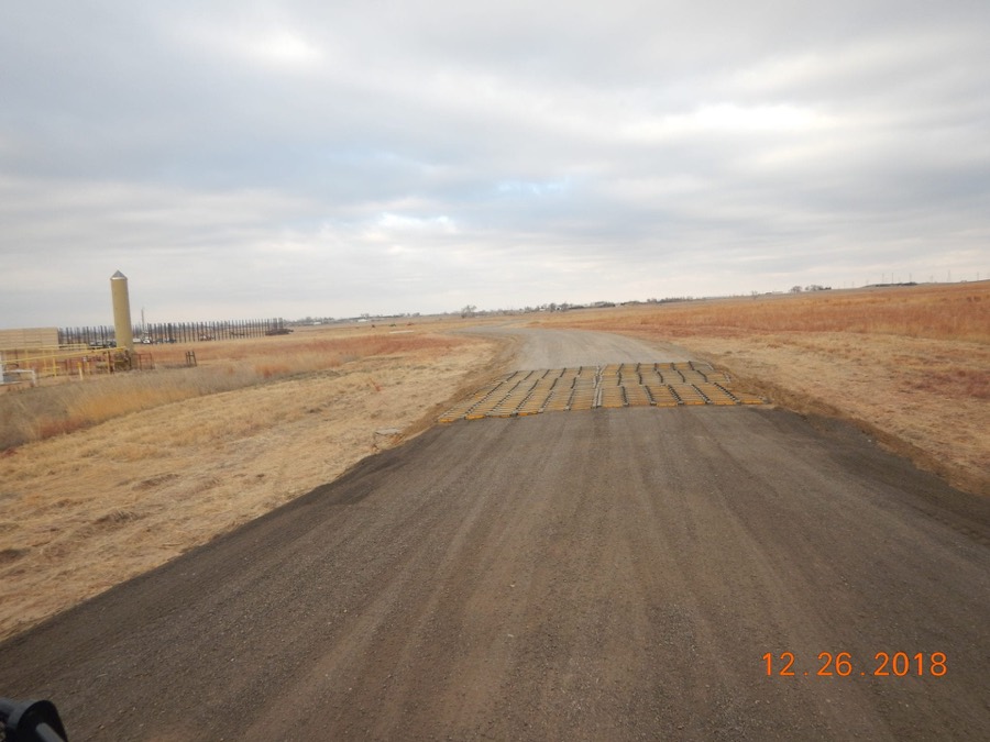 A newly graded access road with a cattle guard running out across Wyoming grassland toward a well site