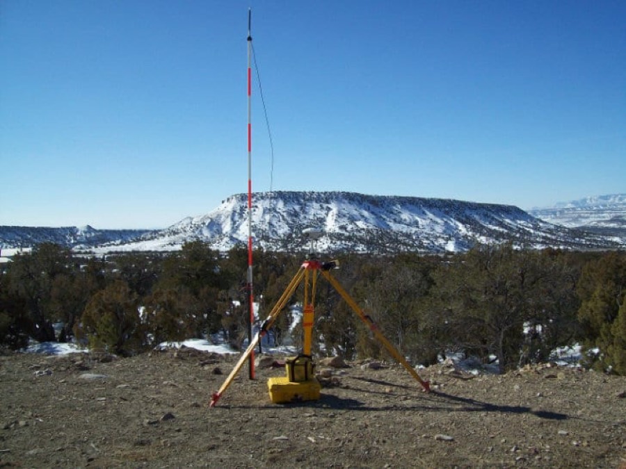 A survey base station on a tripod overlooking a snow-covered mesa
