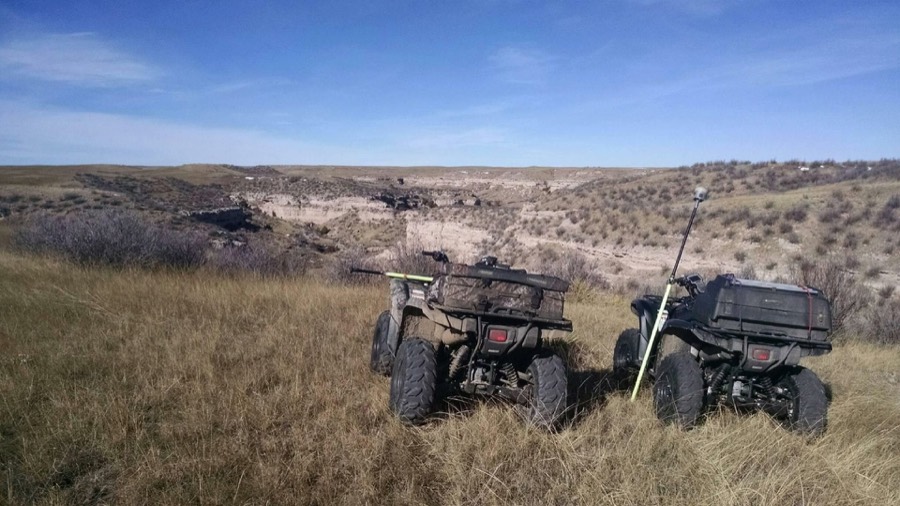 Two survey ATVs loaded with equipment parked on a grass bench above a Wyoming draw
