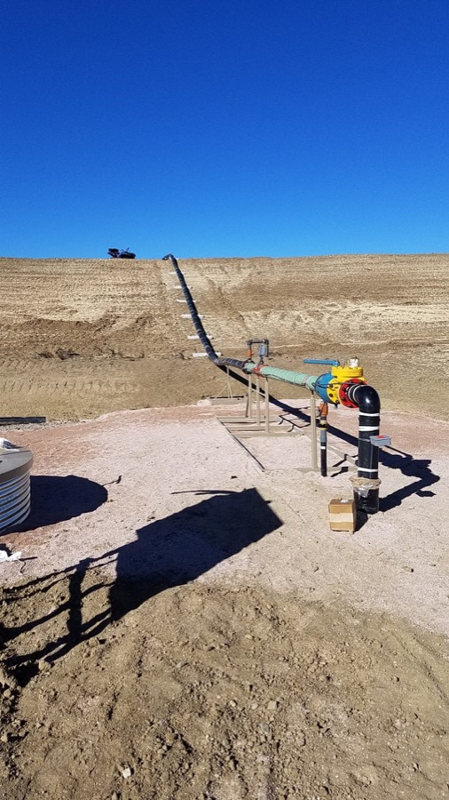 A buried water line rising out of a lined pond to a valve manifold